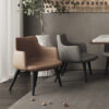 Modern seating area with tan and gray armchairs around a wooden table a potted plant nearby and nuts scattered on the rug