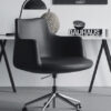 Black swivel office chair on casters in a minimalist workspace with a white desk and Bauhaus book on top