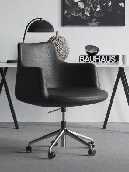 Black swivel office chair on casters in a minimalist workspace with a white desk and Bauhaus book on top